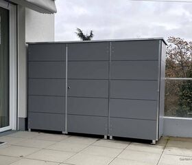 Metall-Gartenbox auf Balkon, grau, modern, neben Glasscheibe und Hauswand.