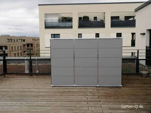 Eine moderne Terrasse mit Geländer und grauem Geräteschrank im Vordergrund, Gebäude im Hintergrund.