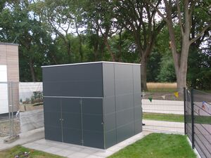 Ein schwarzes Gebäude im Freien, umgeben von Bäumen und einem Zaun, mit einem Banner im Hintergrund.