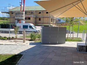 Baustelle mit Baugerüst, Lieferwagen und Betonmischer vor einem Haus in Arbeit. Im Vordergrund Pflanzungen.