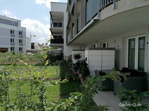 Moderne Wohnung mit Balkon, Gartenbereich und Gartenmöbeln; im Hintergrund weitere Gebäude und ein Kran.